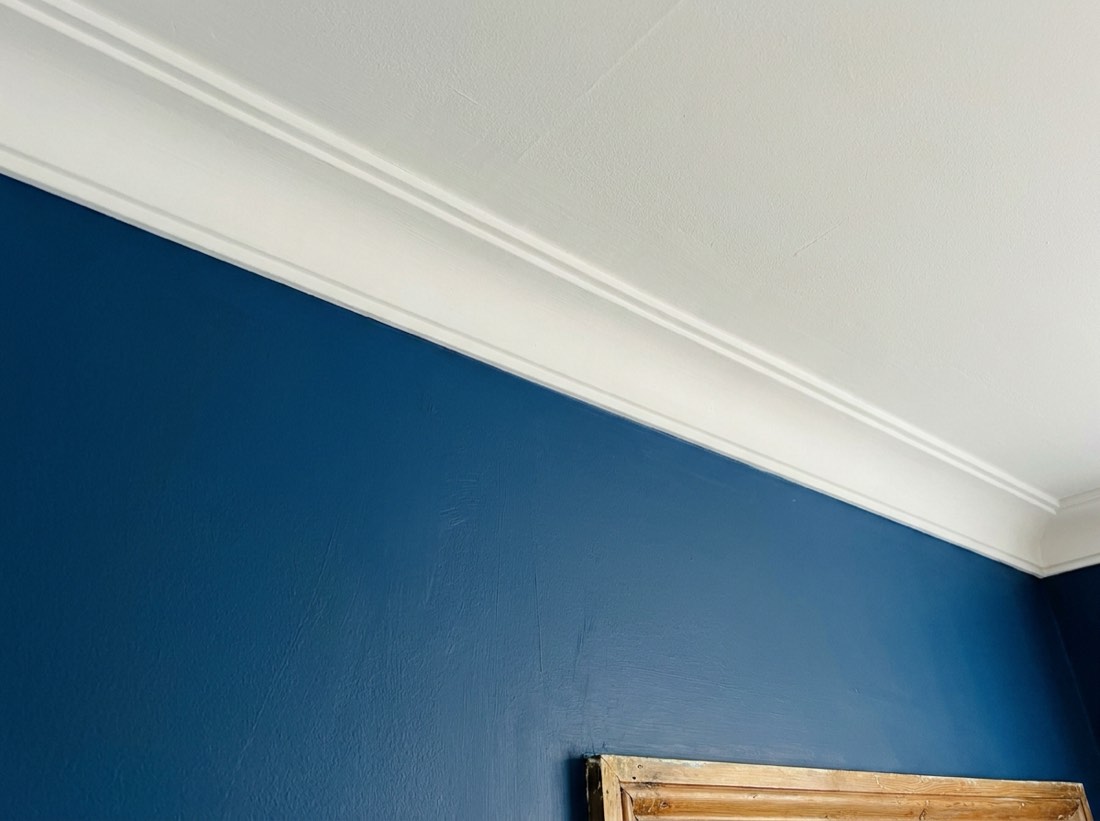 Close-up of a straight hand-painted line where a deep blue wall meets white coving
