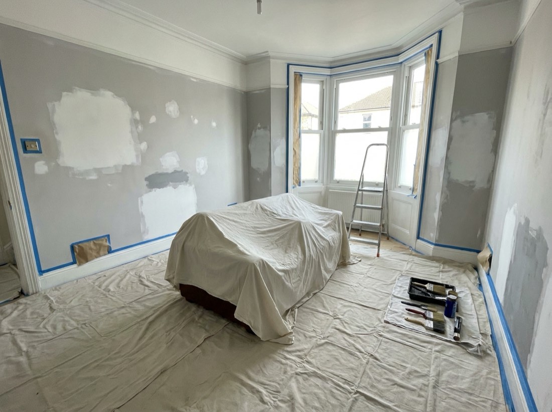Living room prepared for decorating with furniture and floor under dust sheets and edges masked